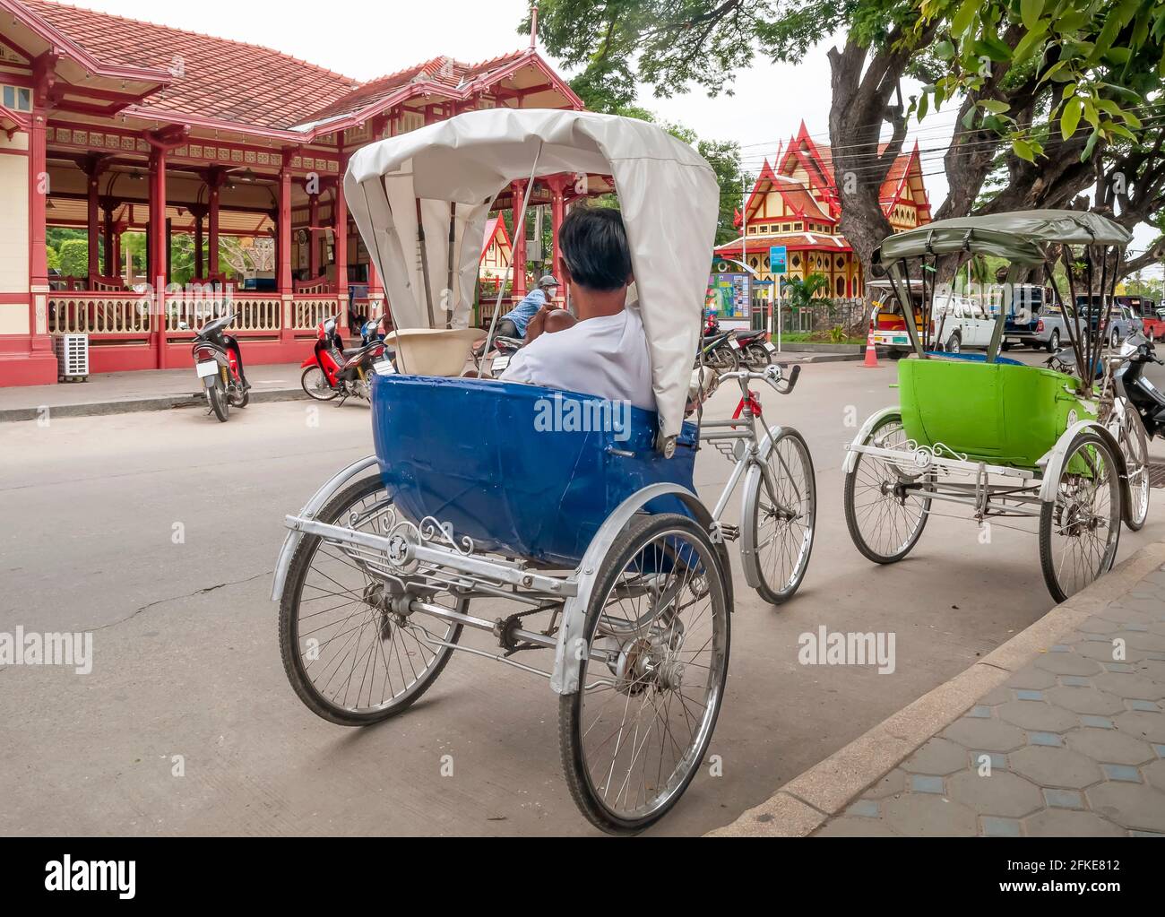 I colorati samlor attendono i clienti di essere trasportati fuori dalla splendida stazione ferroviaria di Hua Hin, in Thailandia Foto Stock