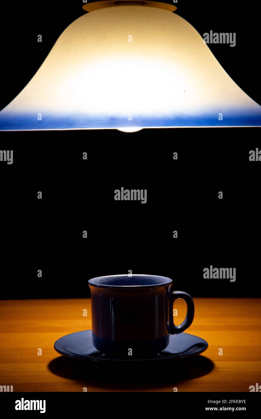 Un teacup sul tavolo sotto un lampadario di luce, su uno sfondo nero Foto Stock