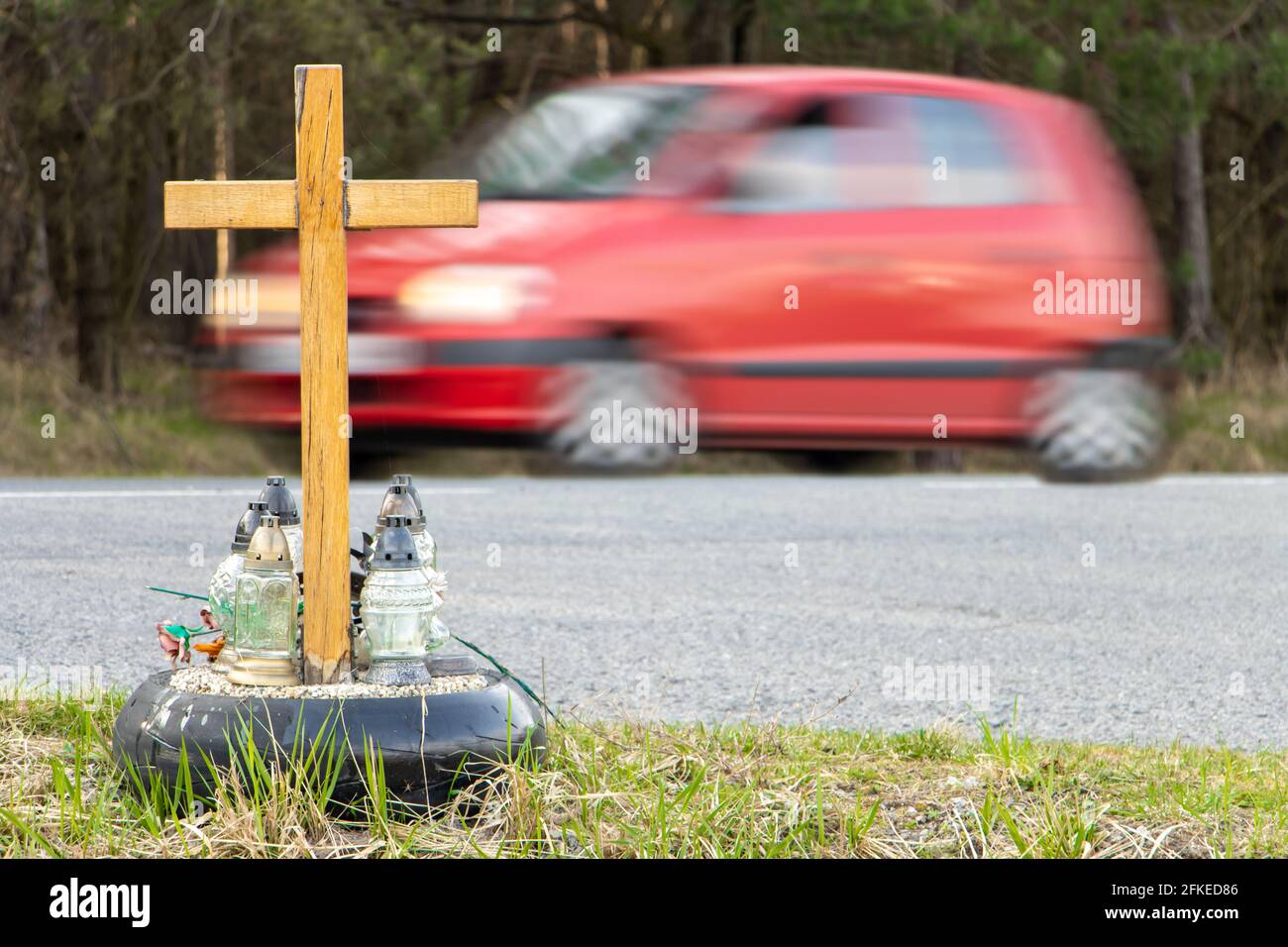 Una croce commemorativa a bordo strada con candele che commemorano la tragica morte, su un giro di fondo auto offuscata. Foto Stock