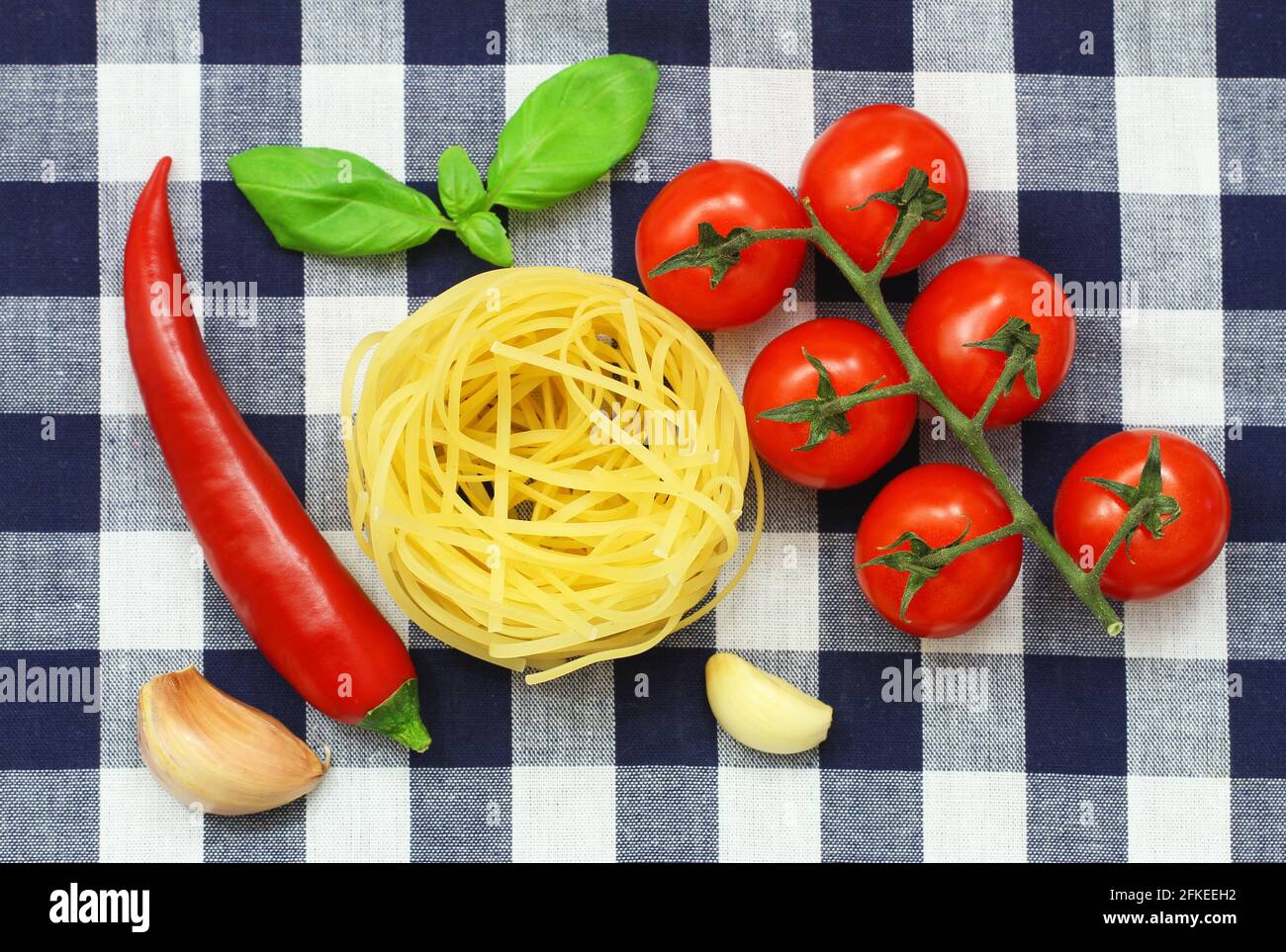 Selezione di ingredienti di pasta: Tagliatelle, pomodori ciliegini, aglio, peperoncino e foglie di basilico fresco Foto Stock