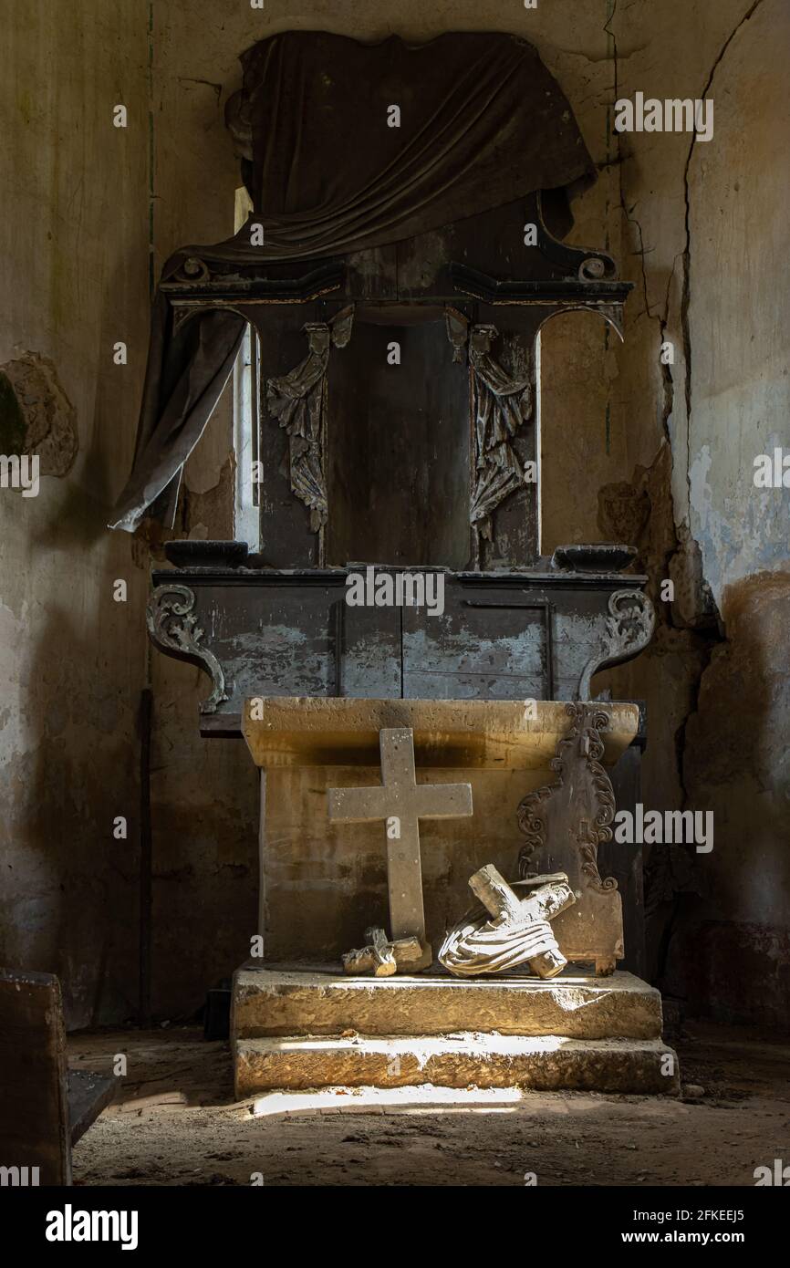 L'altare danneggiato nella chiesa con luce solare sulla croce caduta. Foto Stock