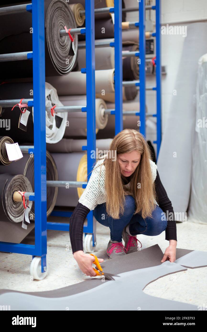 Giovane donna che taglia un pezzo di tappeto in un negozio di tappezzeria. Concetto di lavoro. Foto Stock