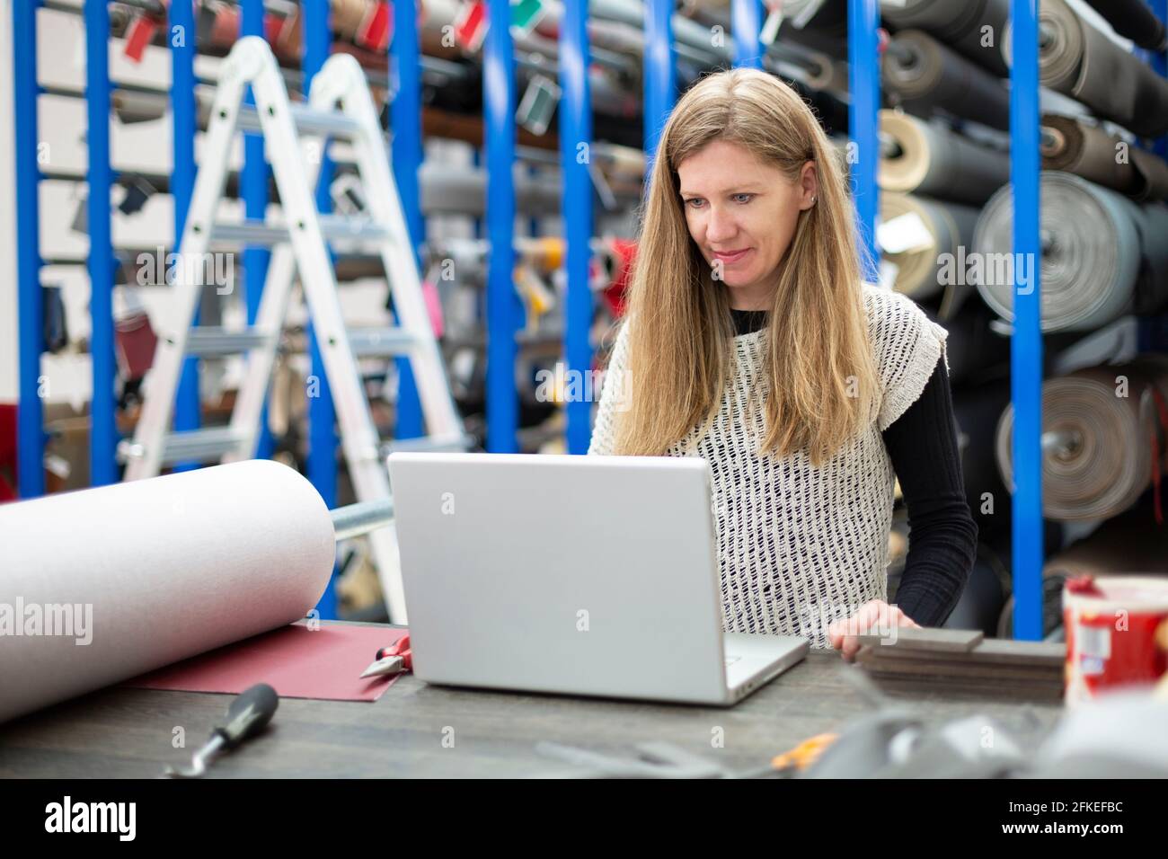 Giovane donna caucasica che lavora con il suo laptop in una fabbrica tessile. Concetto di tecnologia e industria. Foto Stock