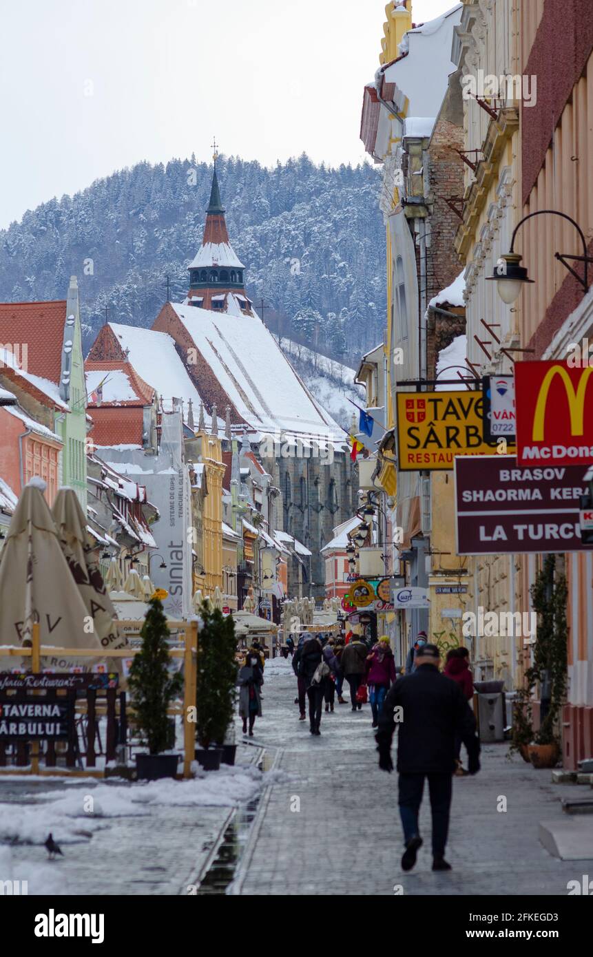 Gli amanti dello shopping tra la neve primaverile in strada Republicii nel centro storico di Brasov Romania. La famosa Chiesa Nera è prominente sullo sfondo - pH Foto Stock