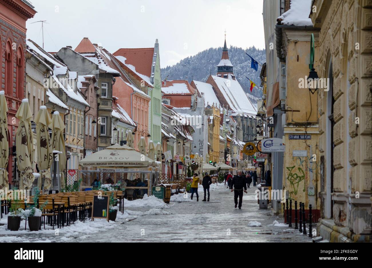Gli amanti dello shopping tra la neve primaverile in strada Republicii nel centro storico di Brasov Romania. La famosa Chiesa Nera è prominente sullo sfondo - pH Foto Stock