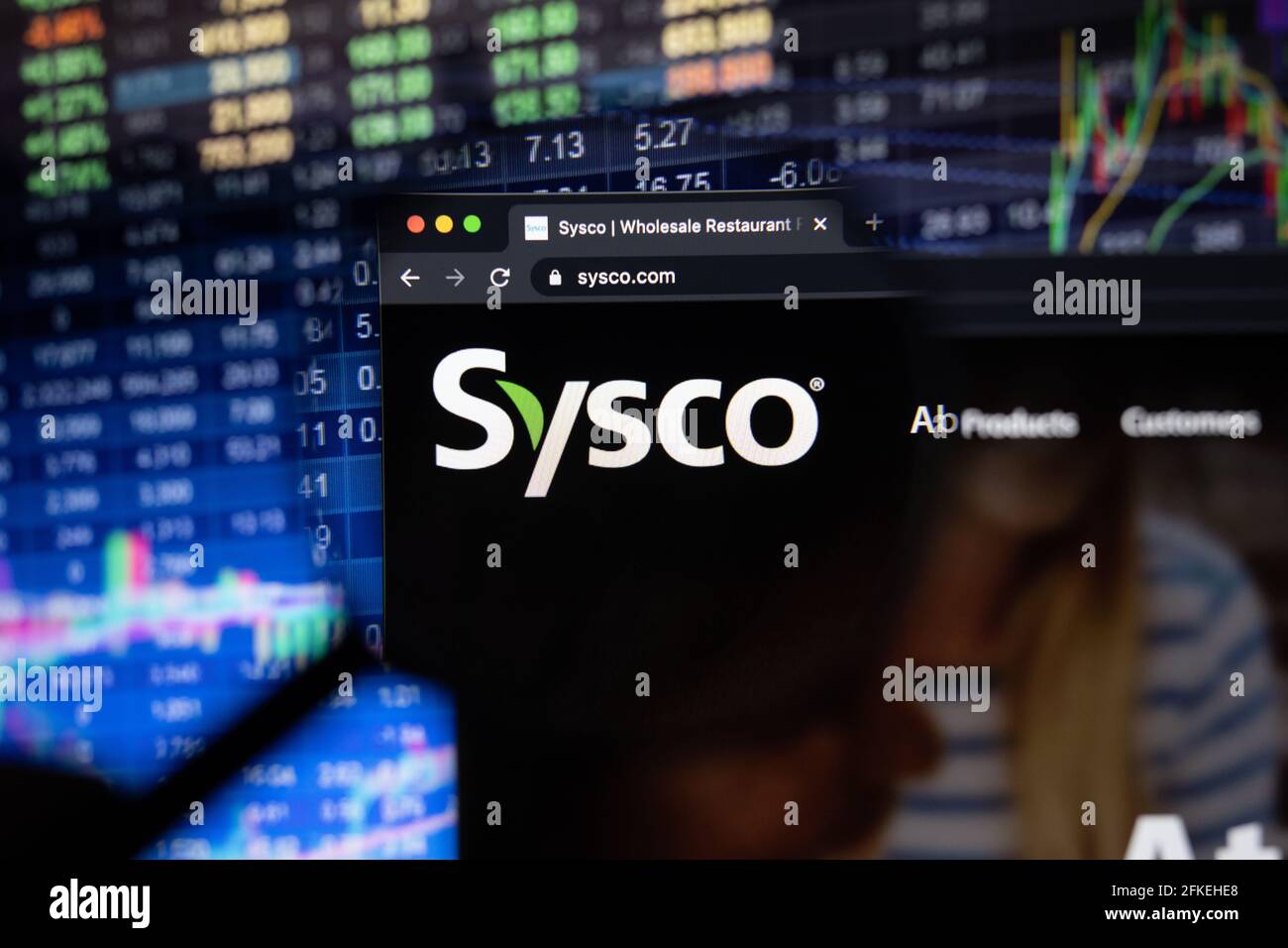 Sysco logo aziendale su un sito web con sviluppi sfocati del mercato azionario in background, visto su uno schermo del computer attraverso una lente di ingrandimento Foto Stock