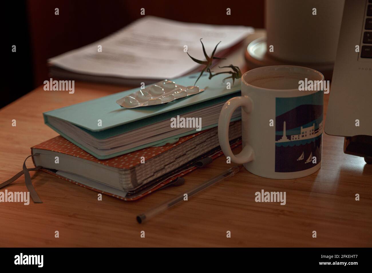 Diario e taccuini su un tavolo accanto a un computer portatile con tazza di caffè, stocchi di pomodoro e pacchetto di pillole vuoto - un lavoro da casa prima colazione Foto Stock