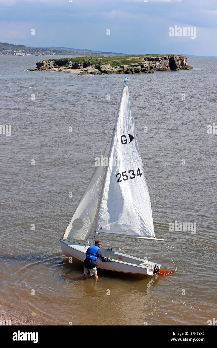 Sailor in GP14 Dingy Lands su Hilbre Island a High Tide con vista attraverso il Medio occhio, Dee Estuary, Wirral, Regno Unito Foto Stock