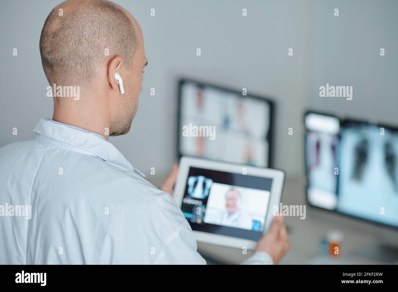 Il medico indossa gli auricolari quando effettua una videochiamata al suo collega da un'altra clinica Foto Stock