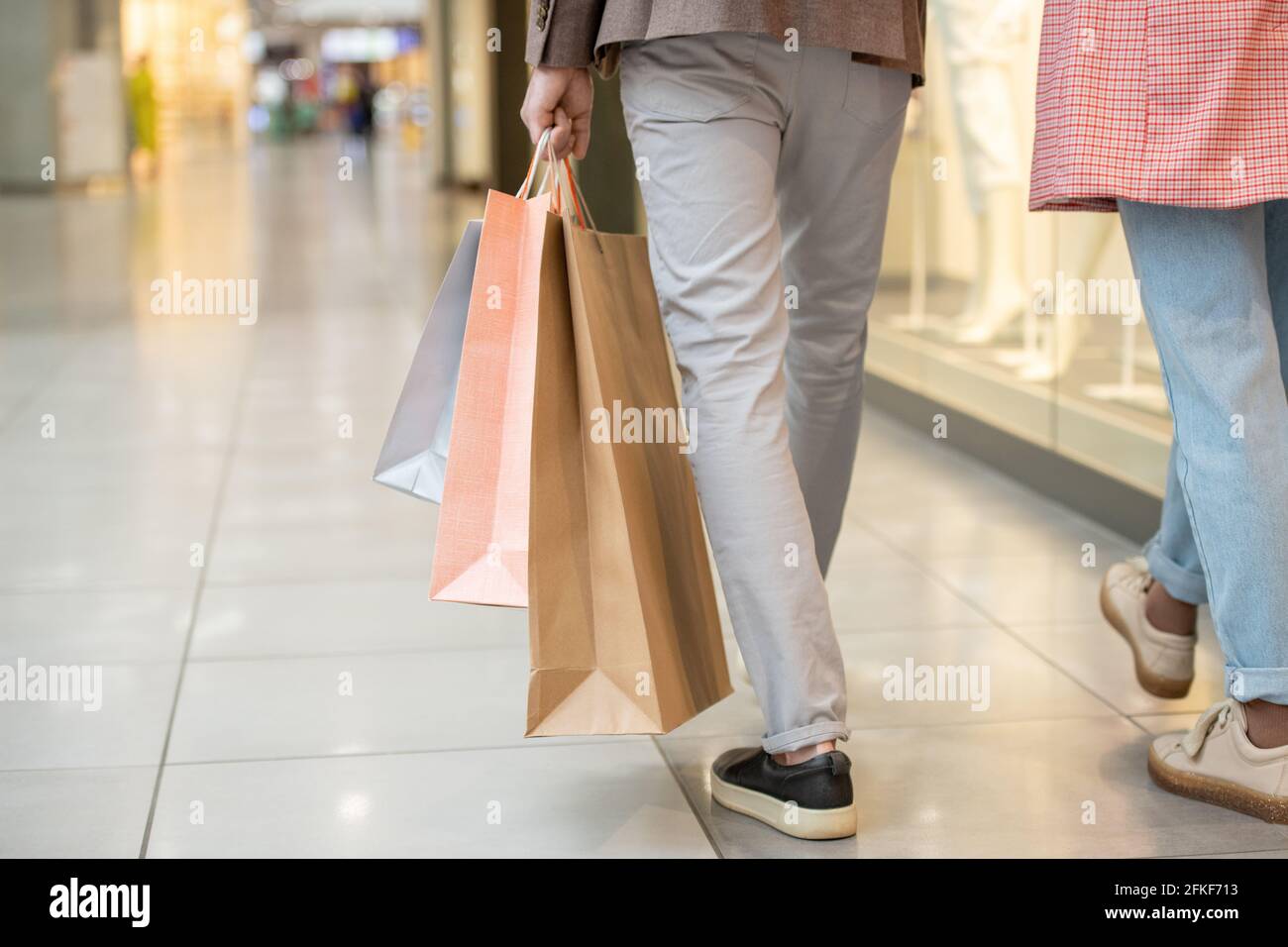 Uomo che trasporta borse per la spesa mentre si sposta all'interno del centro commerciale Foto Stock