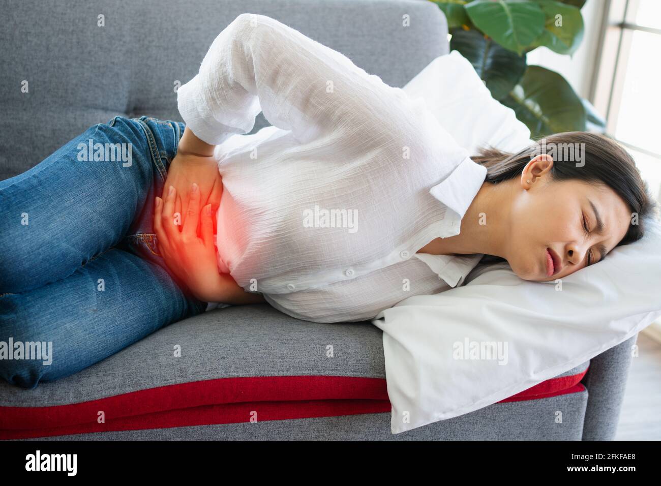 Infelice donna asiatica seduta sul divano e tenuta sulla sofferenza dello  stomaco. Dolore addominale che deriva da mestruazioni, diarrea o  indigestione. Sickn Foto stock - Alamy