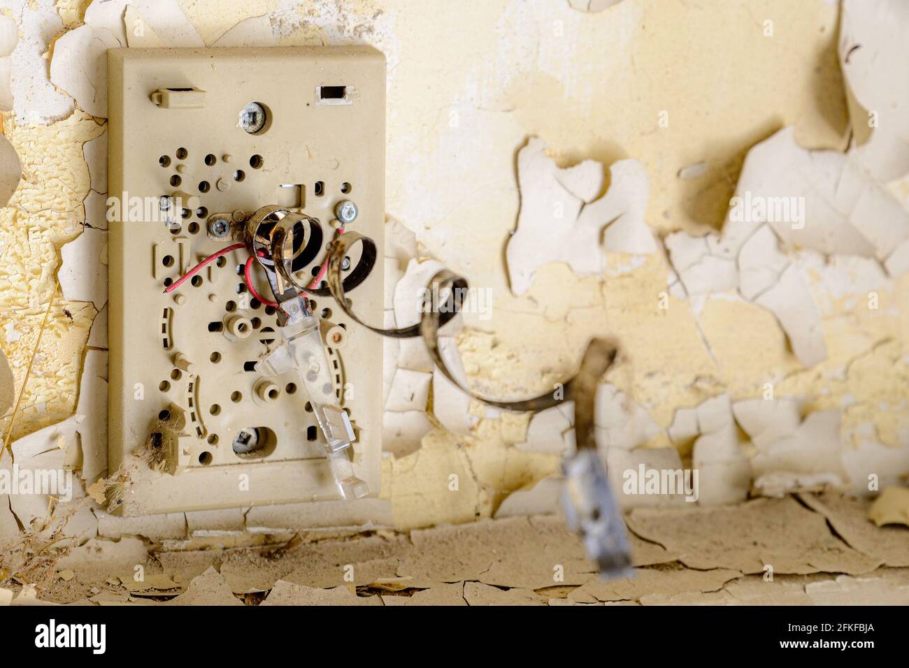 Un termostato bimetallico danneggiato sul muro in un edificio scolastico abbandonato. La molla a spirale metallica è tesa. Profondità di campo poco profonda. Foto Stock