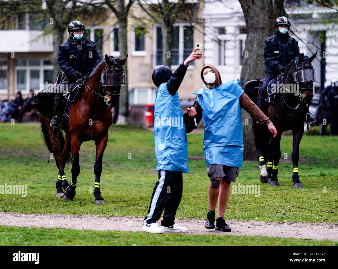 Amburgo, Germania. 01 Maggio 2021. I dimostranti prendono un selfie nel distretto di St. Georg sullo sfondo dello squadrone equestre della polizia. Per il 1° maggio, gruppi di sinistra ed estrema sinistra hanno annunciato numerosi incontri e processioni durante tutto il giorno, soprattutto nella zona del centro della città e dei quartieri limitrofi. Credit: Axel Heimken/dpa/Alamy Live News Foto Stock