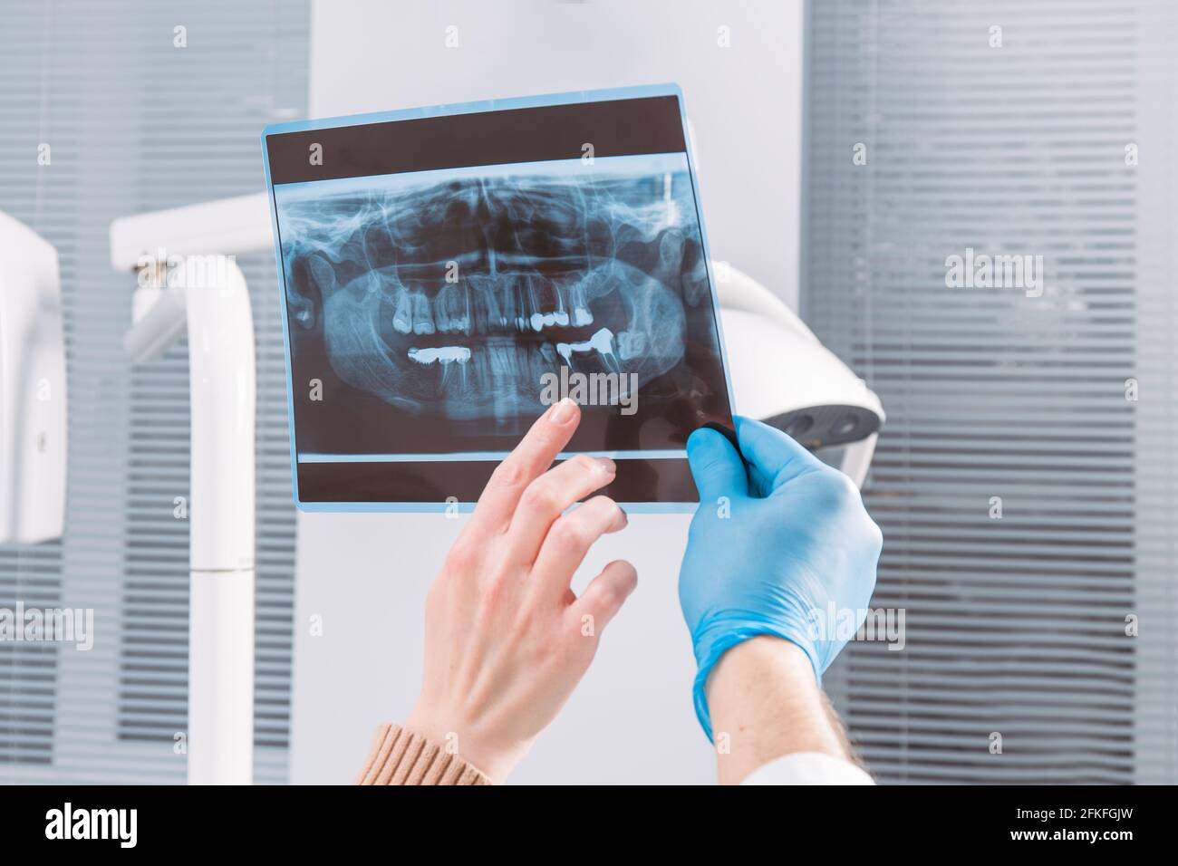 Il medico mostra un'immagine radiografica per il paziente. Primo piano. Le mani del medico nei guanti trattengono l'immagine radiografica della mascella del paziente Foto Stock