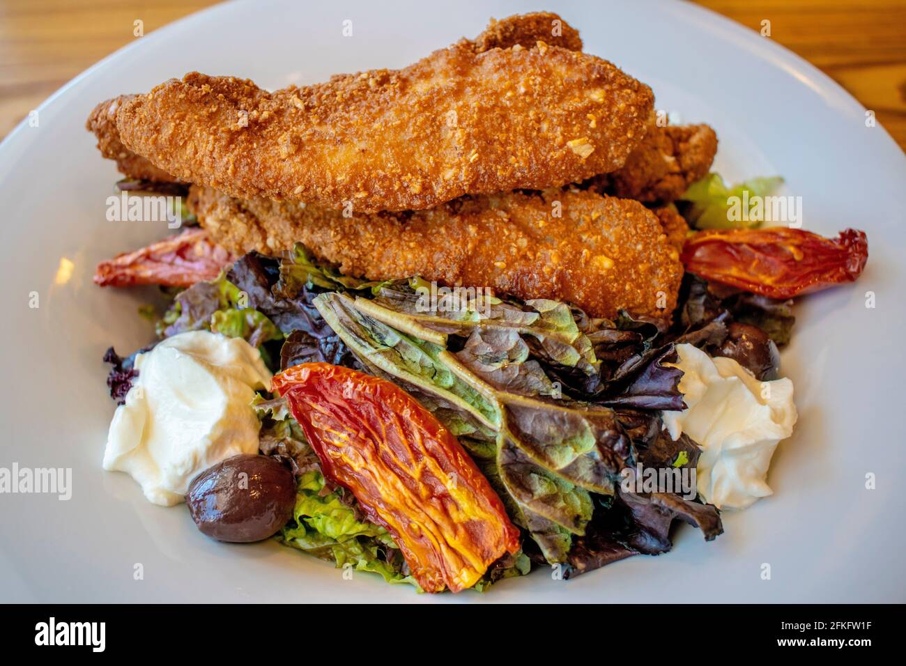 Insalata croccante di pollo (foglie verdi, pollo fritto, formaggio finlandese, pomodori canditi e olive nere). Foto Stock