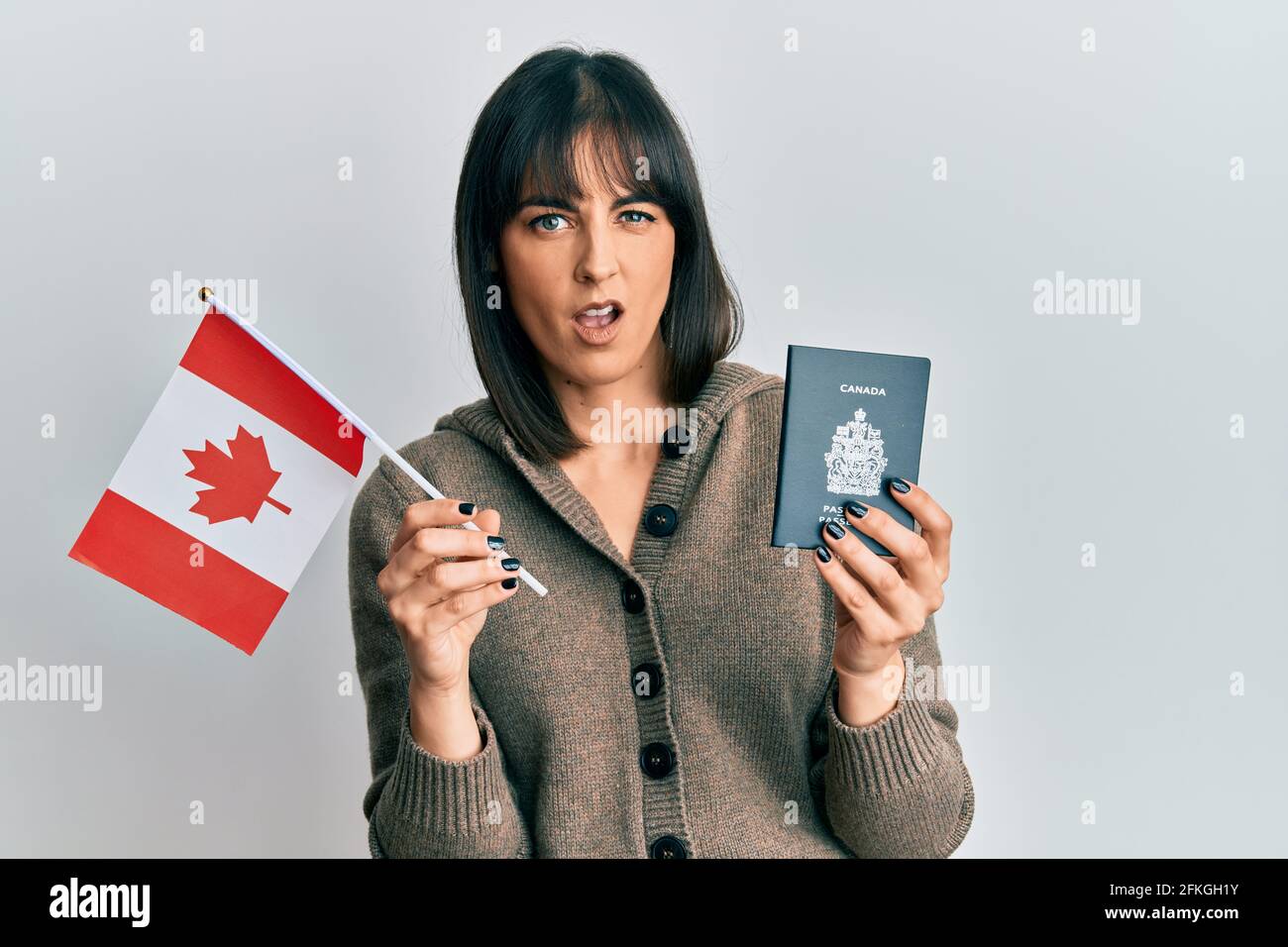 Giovane donna ispanica che detiene bandiera canada e passaporto indistinta e confuso espressione. Dubbio concetto. Foto Stock