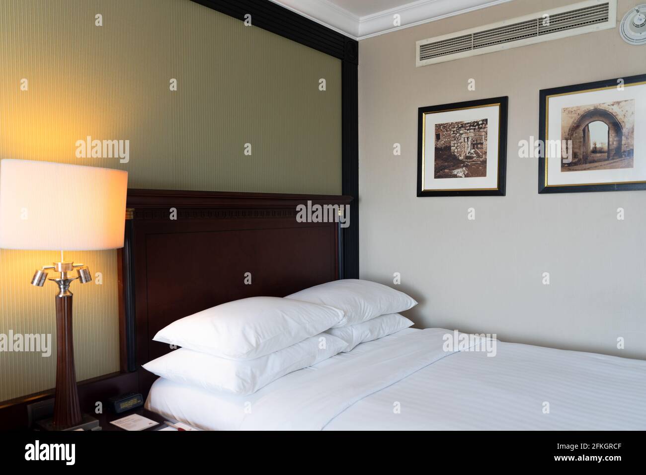 Moderna camera da letto interna dell'hotel con letto appena fatto, testiera, cuscini, illuminazione accanto al letto, opere d'arte sulle pareti Foto Stock