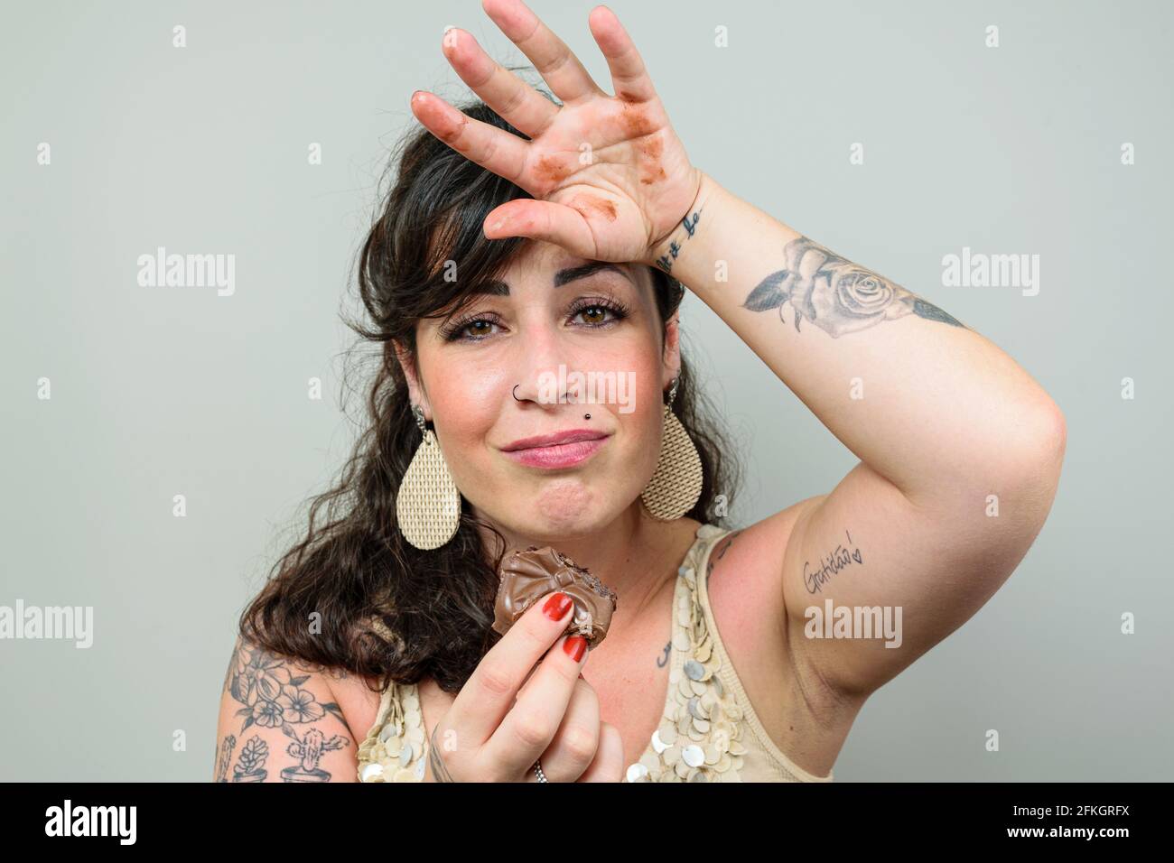 Donna tatuata, guardando la macchina fotografica, con la mano sulla testa e spiacente che ha mangiato una torta brasiliana di miele. Tatuaggio sul bicipite sinistro scritto in Portu Foto Stock