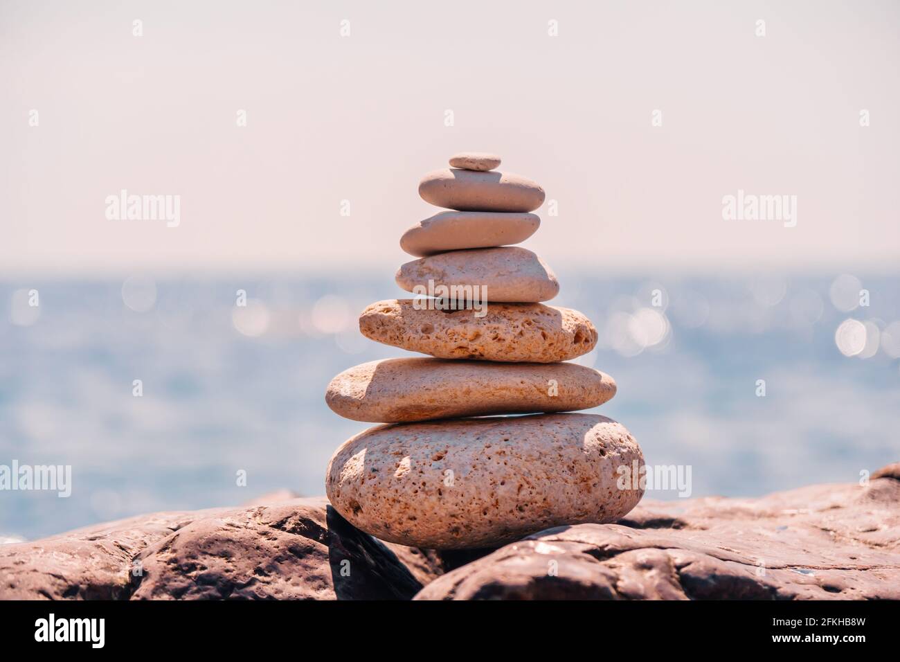 Equilibrata piramide di ciottoli sulla spiaggia in una giornata di sole. Abstract Sea bokeh sullo sfondo. Messa a fuoco selettiva. Pietre Zen sulla spiaggia di mare, meditazione Foto Stock