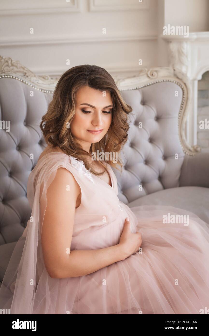 Giovane futura madre seduta sul divano e sorridente Foto Stock