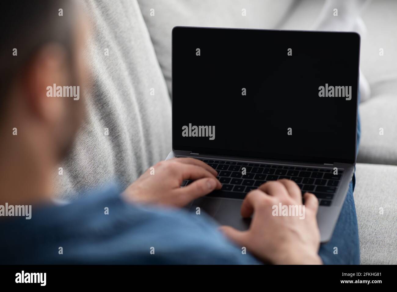 Uomo reclinato sul divano, utilizzando un computer portatile con schermo vuoto Foto Stock