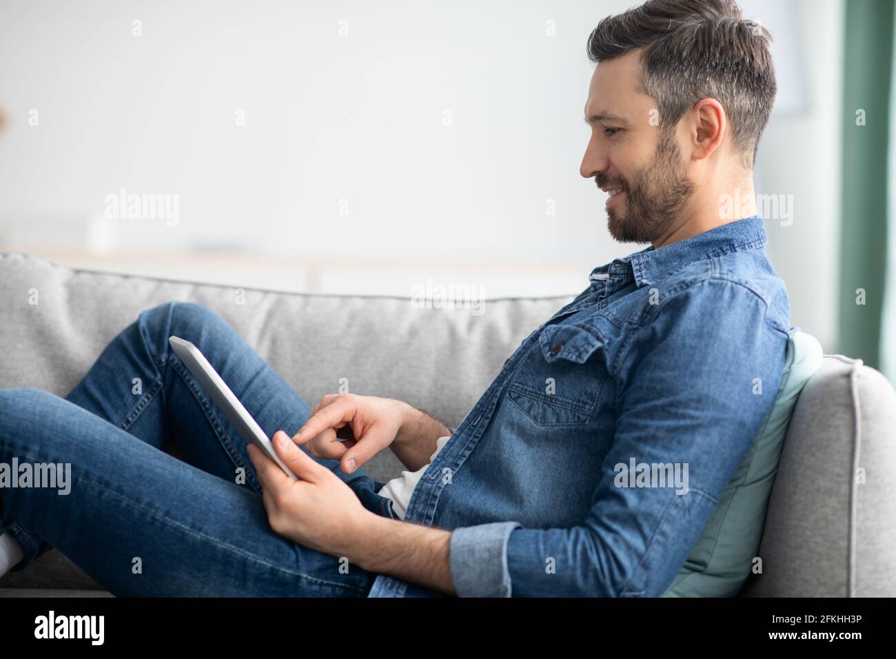 Uomo felice che si distende sul divano a casa, utilizzando un tablet digitale Foto Stock