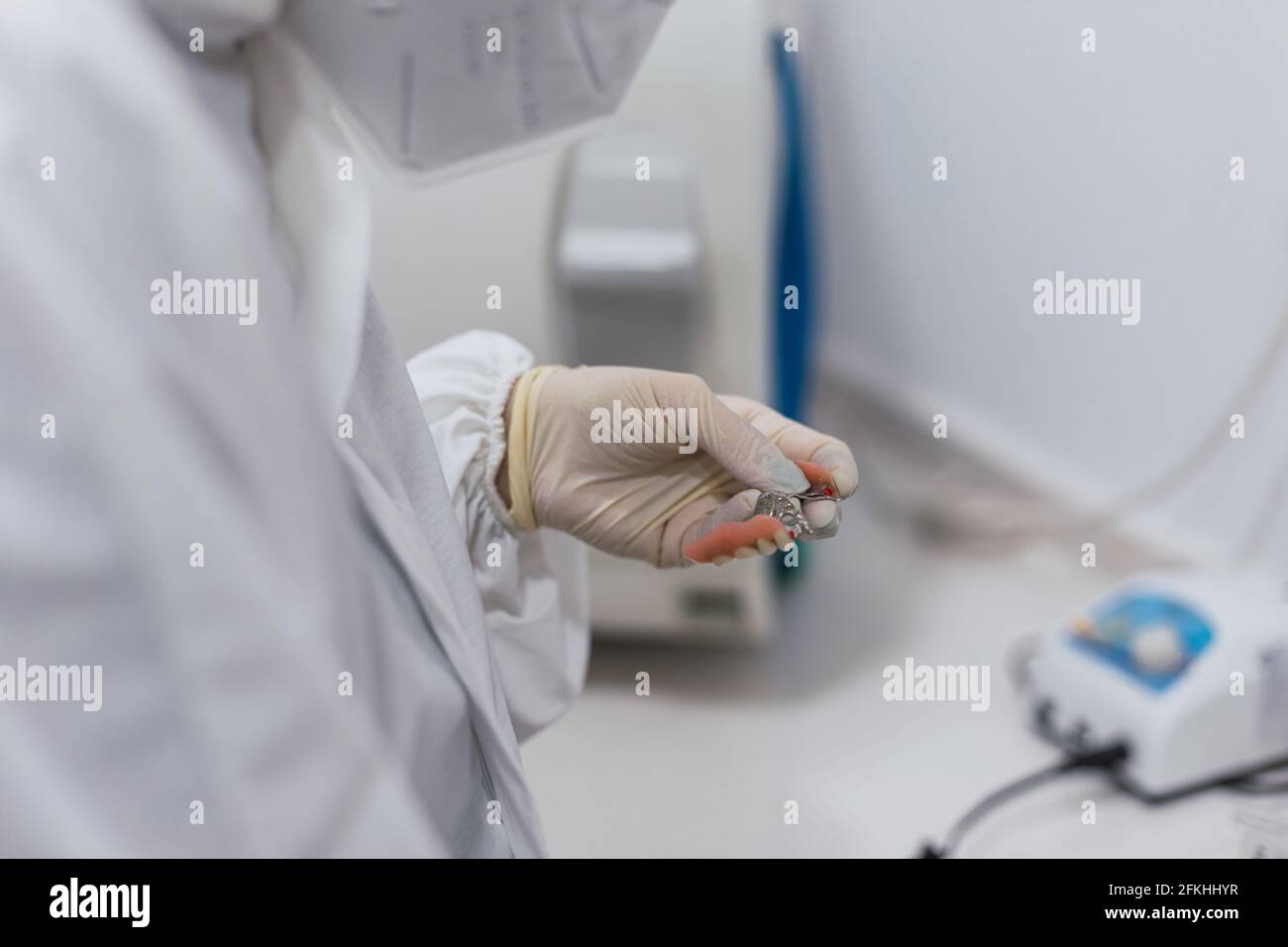 Mani di un tecnico dentale con maschera chirurgica e vetri che lucidano le protesi sulla sua tabella. Concetto di salute Foto Stock