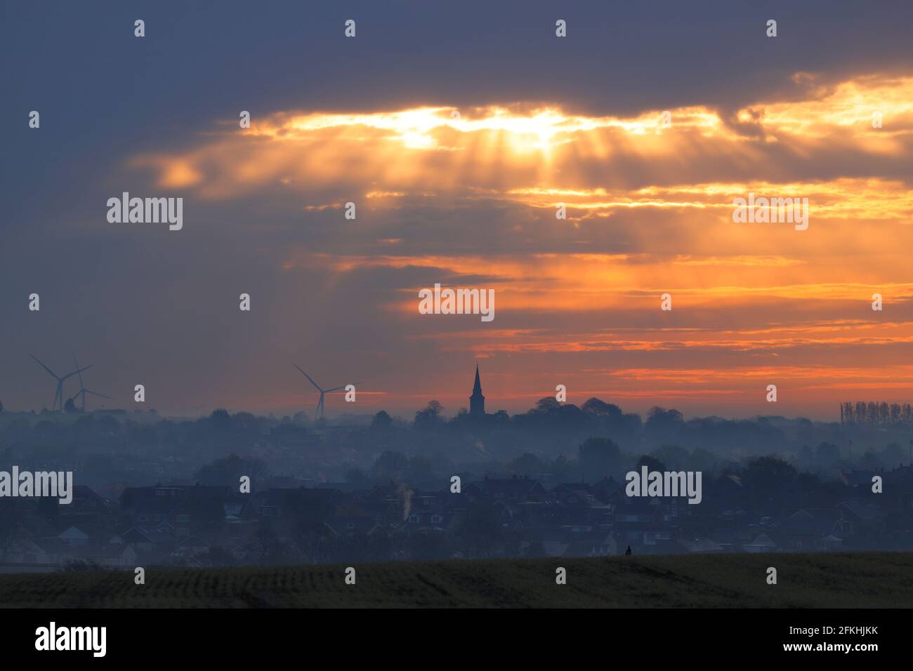 Alba su Garforth a Leeds. La Chiesa di Santa Maria si erge sopra i tetti con turbine eoliche di Hook Moor. Foto Stock