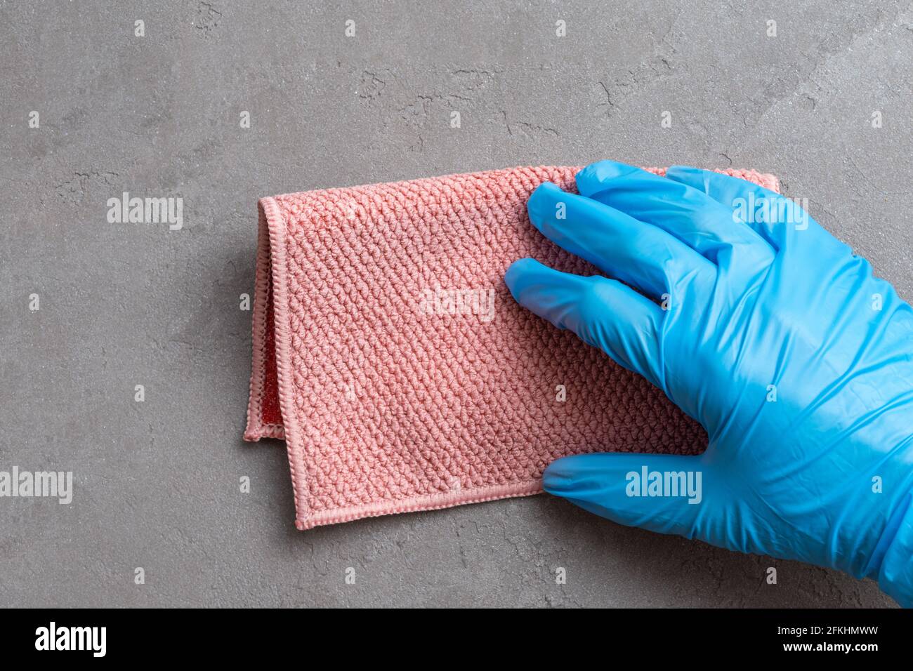 Pulizia della casa. Una mano in un guanto di lattice blu sta sfregando un panno di microfibra rosa su una superficie di intonaco grigio, primo piano. Foto Stock