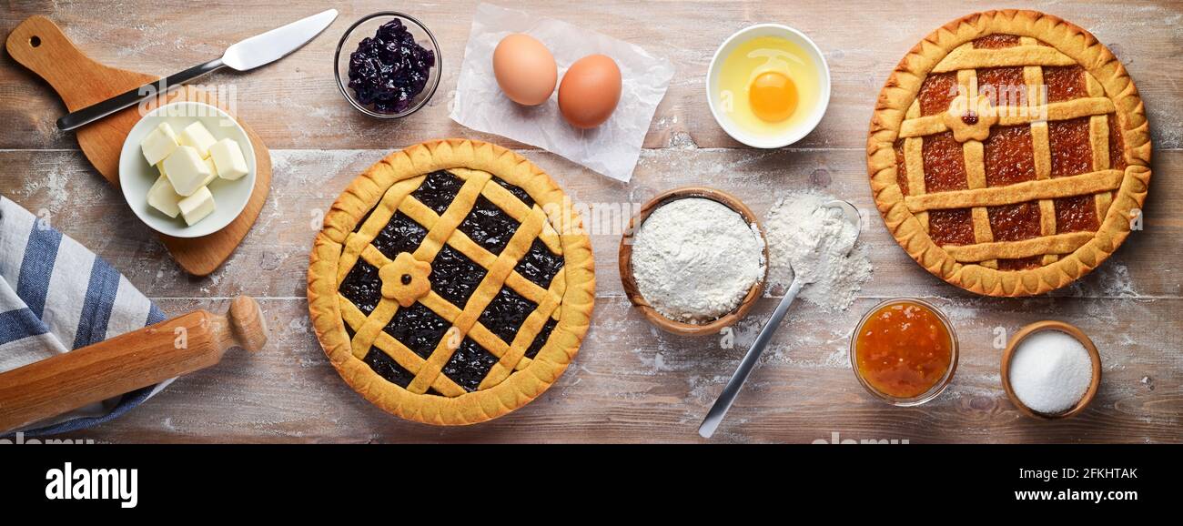 Due crostate, pasta frolla con amarena e marmellata d'arancia, farina, burro, uova e altri ingredienti sulla tavola da pasticceria. Vista dall'alto, disposizione piatta. Foto Stock