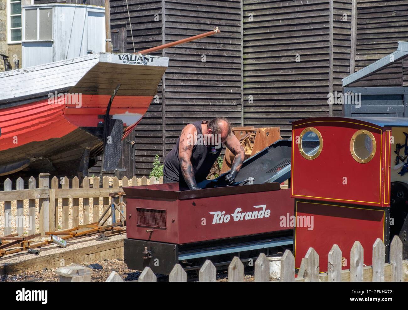 Un uomo con grasso nero sulle sue braccia lavora su motore di ferrovia in miniatura presso lo Stade, Hastings, Old Valiant barca da pesca & Net negozi in background. Foto Stock