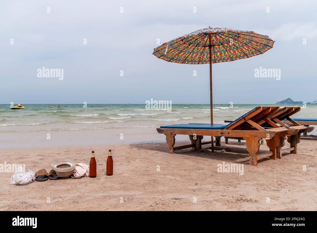 Due lettini, un ombrellone, due bottiglie di birra e vestiti abbandonati sulla sabbia dai turisti che bagnano nel mare di Hua Hin, Thailandia Foto Stock