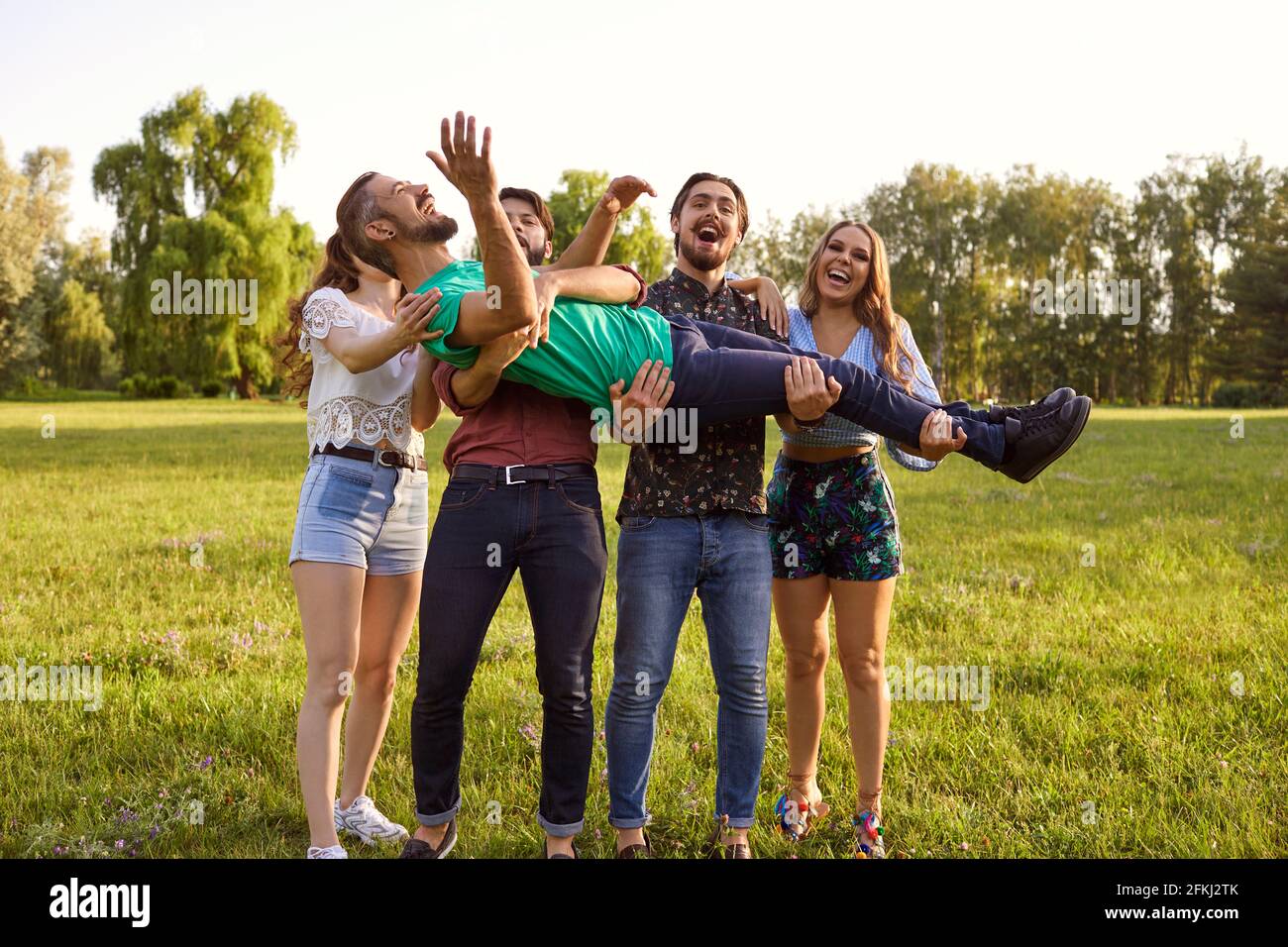 Giovani amici allegri che si divertono in campagna il giorno d'estate. Gruppo di persone che ridono ed essendo sciocco nella natura Foto Stock