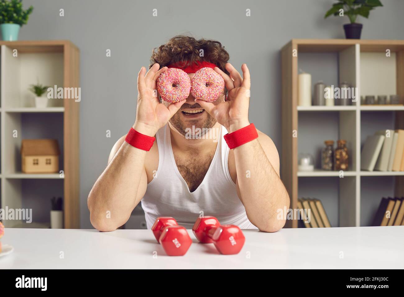 Uomo divertente in sportswear seduto a casa tavolo fare ciambella occhiali ritratto Foto Stock