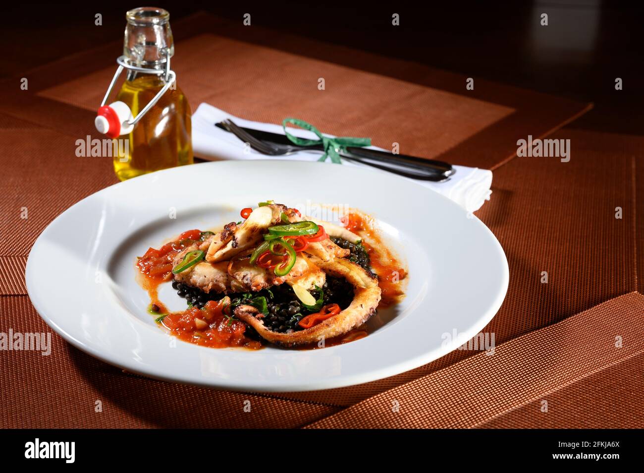 Tentacoli di polpo arrosto con alcune verdure e una piccola bottiglia con olio d'oliva in un raffinato ristorante. Foto Stock
