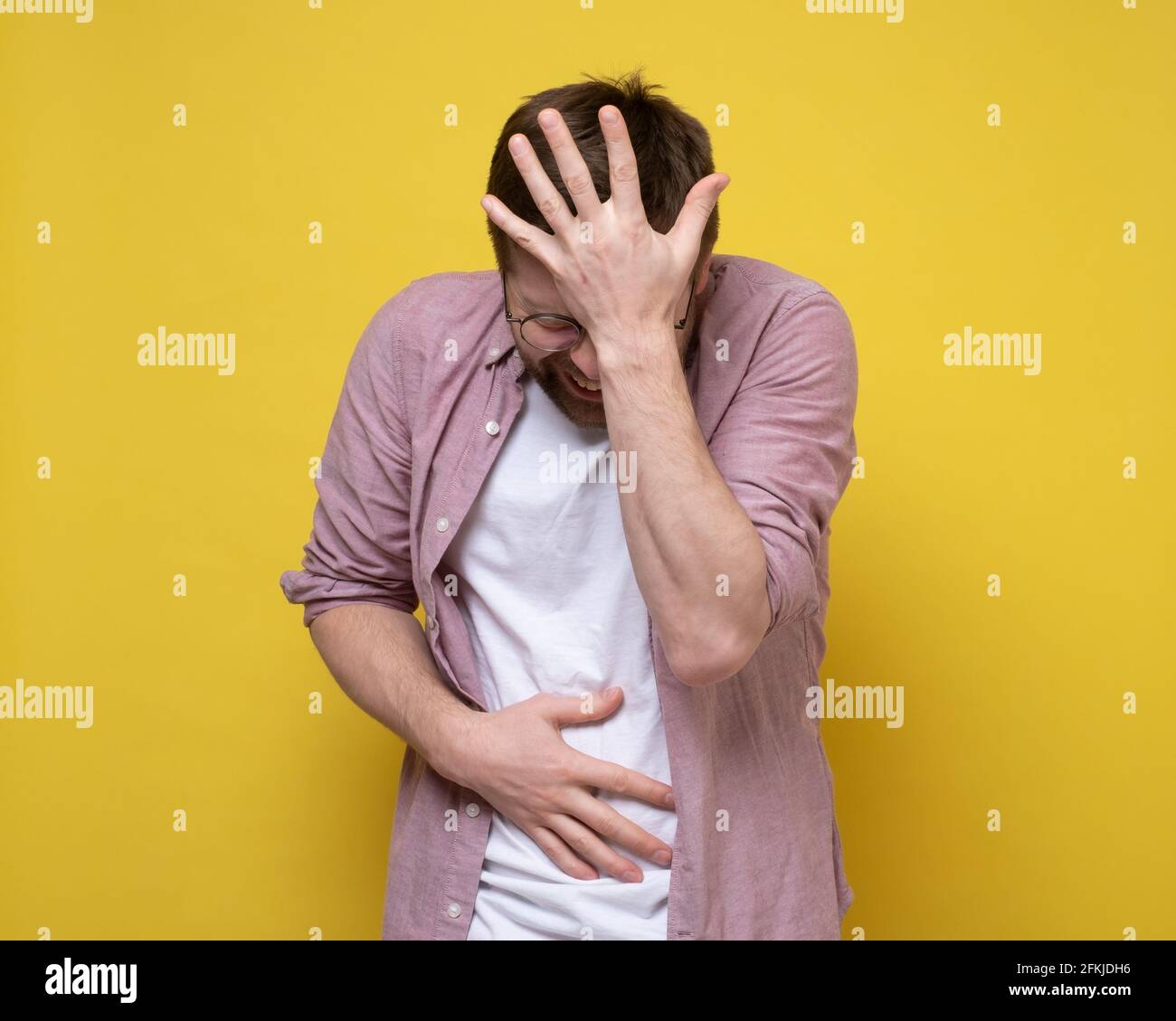 Il giovane sta sperimentando dolore addominale molto grave, soffre tenendo lo stomaco e la testa con le mani. Sfondo giallo. Foto Stock