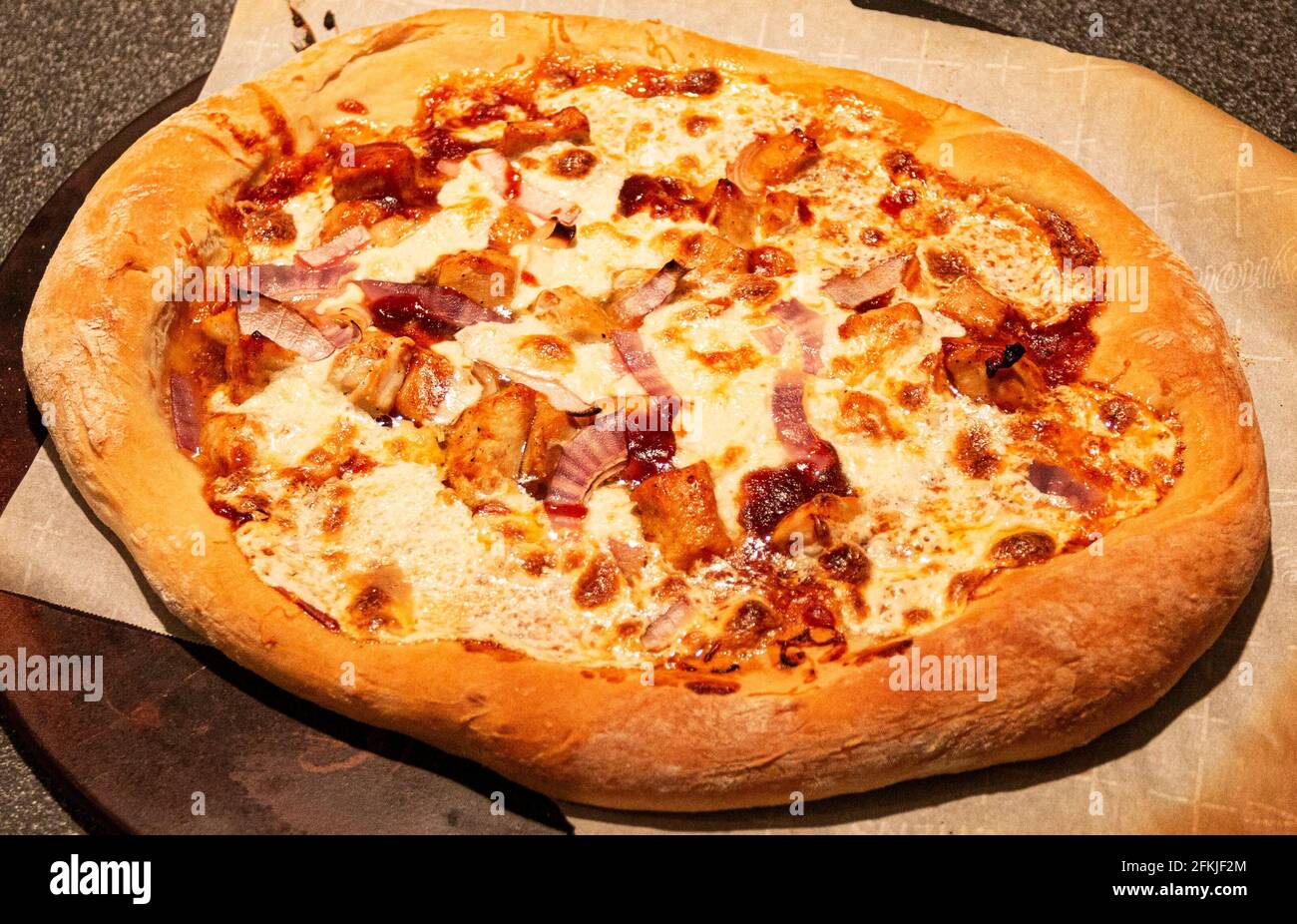 Primo piano di una pizza fatta in casa di pollo barbecue con cipolle rosse  su carta di cera e pietra pizza fresco fuori dal forno Foto stock - Alamy