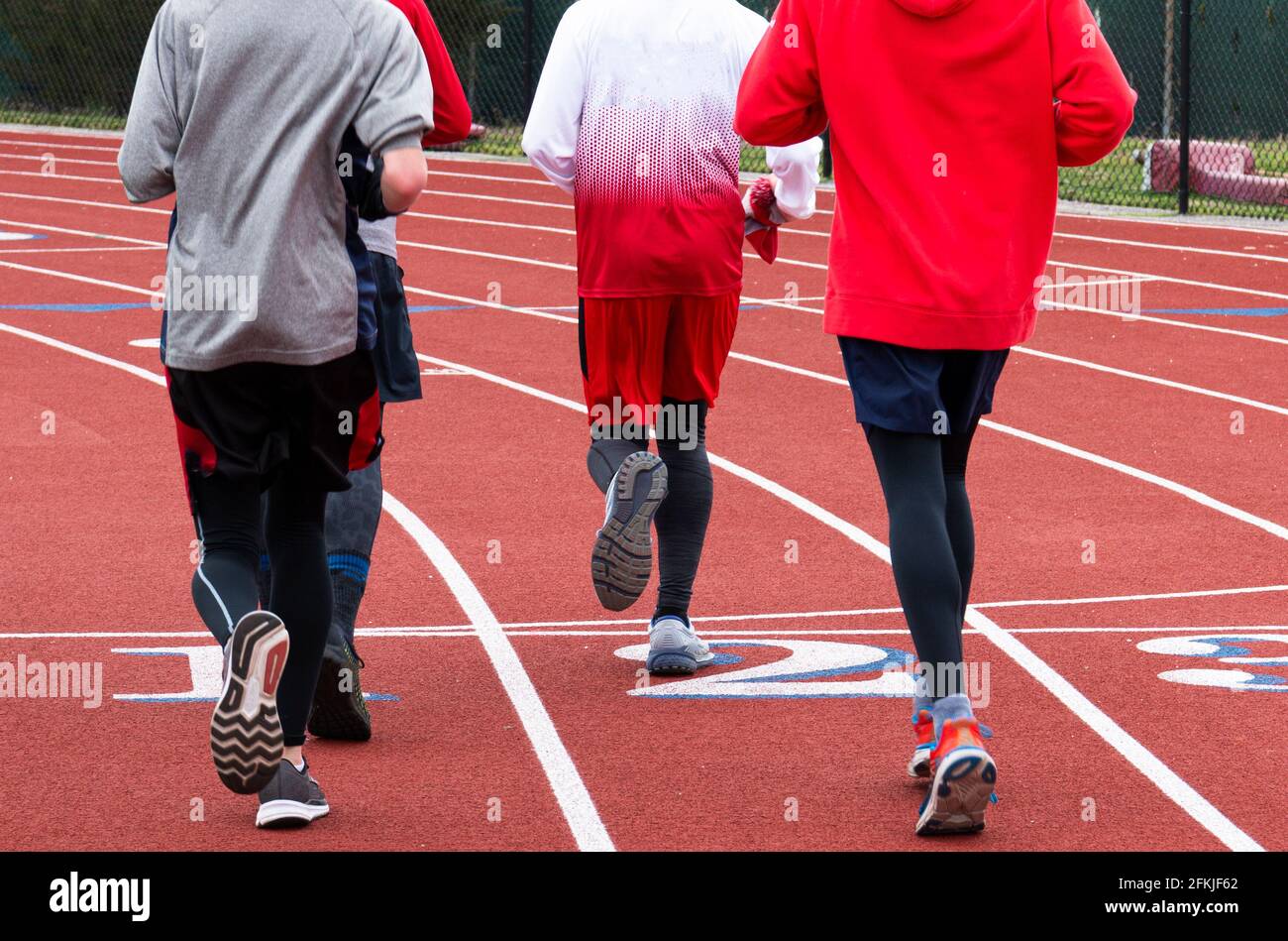 Vista posteriore di quattro corridori della scuola superiore che corrono su una pista che attraversa la linea di arrivo insieme in un gruppo durante la pratica di pista e campo. Foto Stock