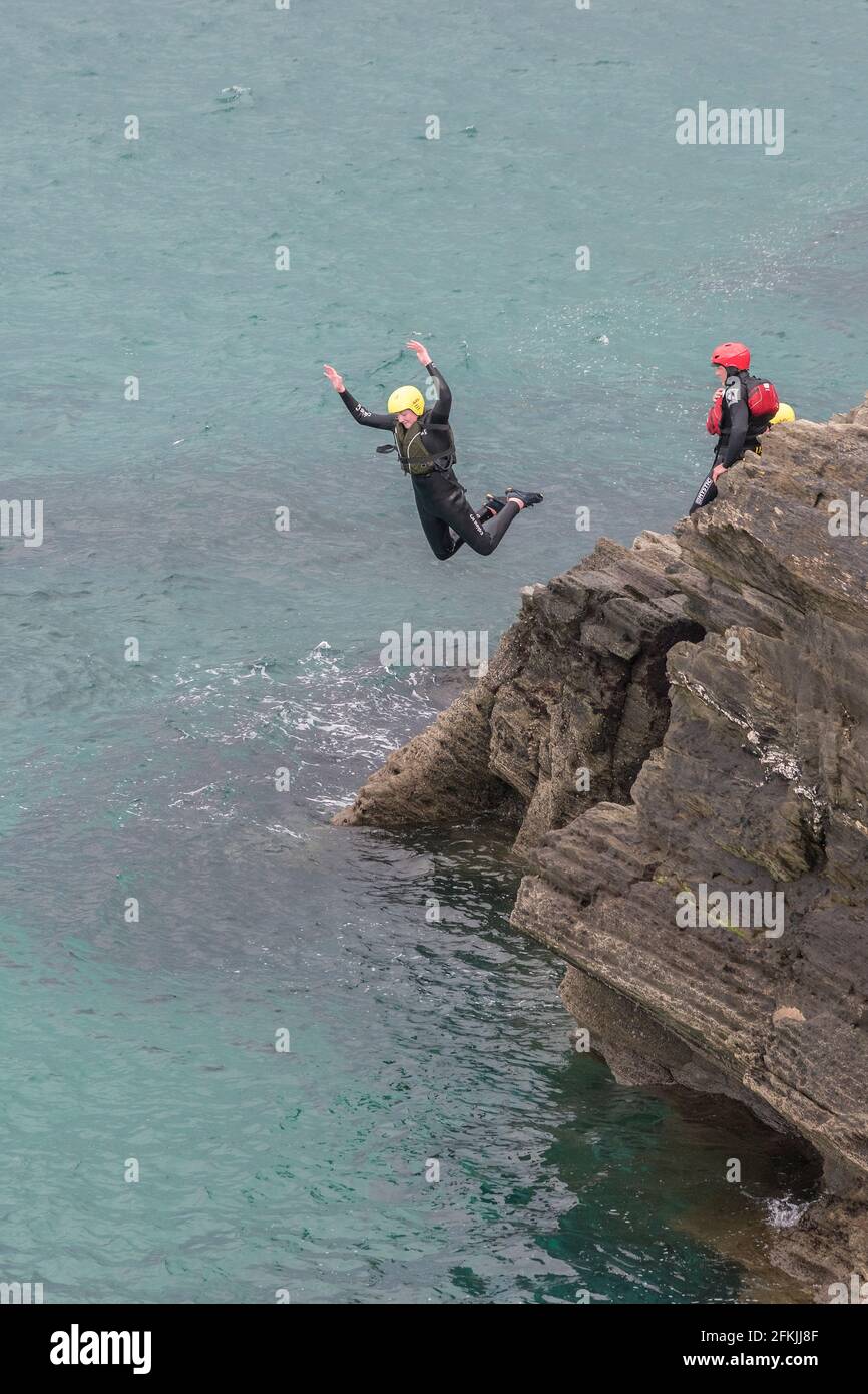 Un turista che salta dalle rocce durante una sessione di coastering intorno alla zona intercorrente a Towan Head a Newquay in Cornovaglia. Foto Stock