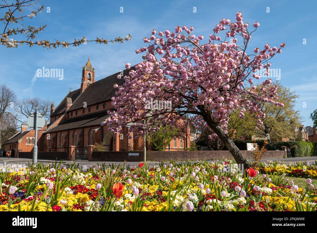Chiesa di San Marco a Farnborough, Hampshire, Regno Unito, durante la primavera con alberi di ciliegio e aiuole colorate. Foto Stock