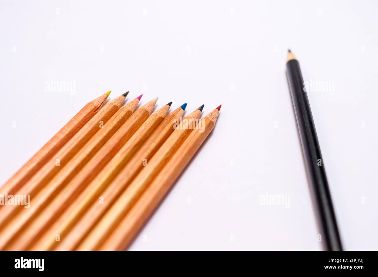 Sfondo bianco con una disposizione di matite colorate e una matita nera separata. Con un campo di testo grande Foto Stock
