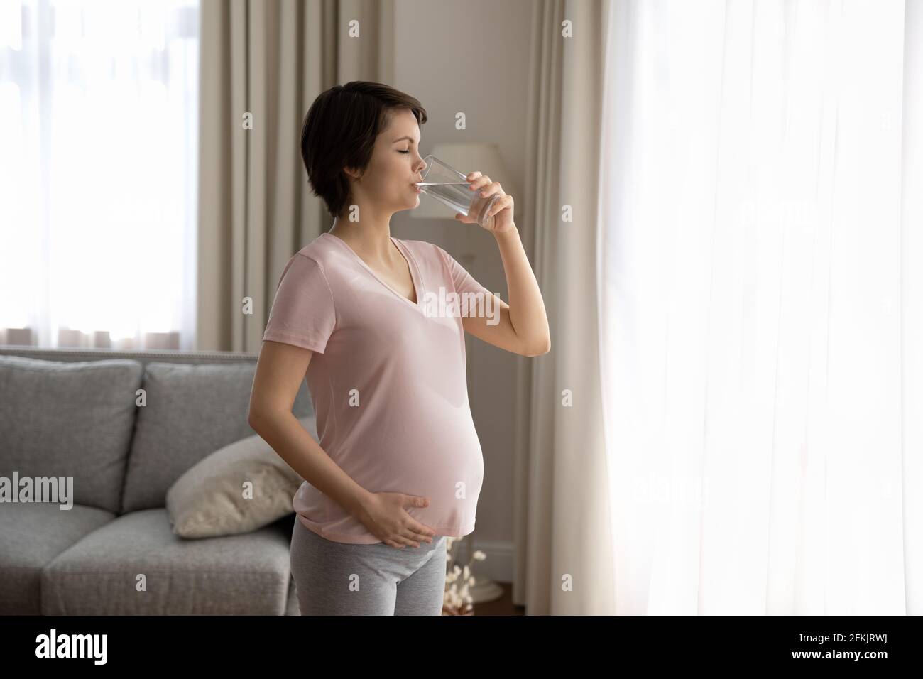 Donna incinta bere ancora acqua pulita dal vetro Foto Stock