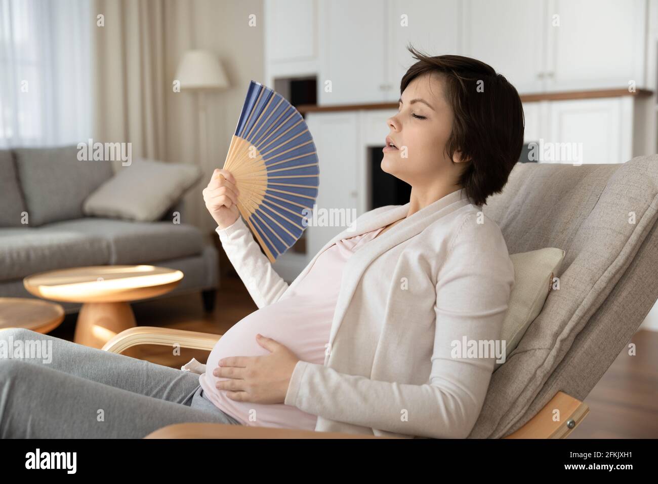 Donna incinta stanca usare il ventilatore della mano a casa Foto Stock