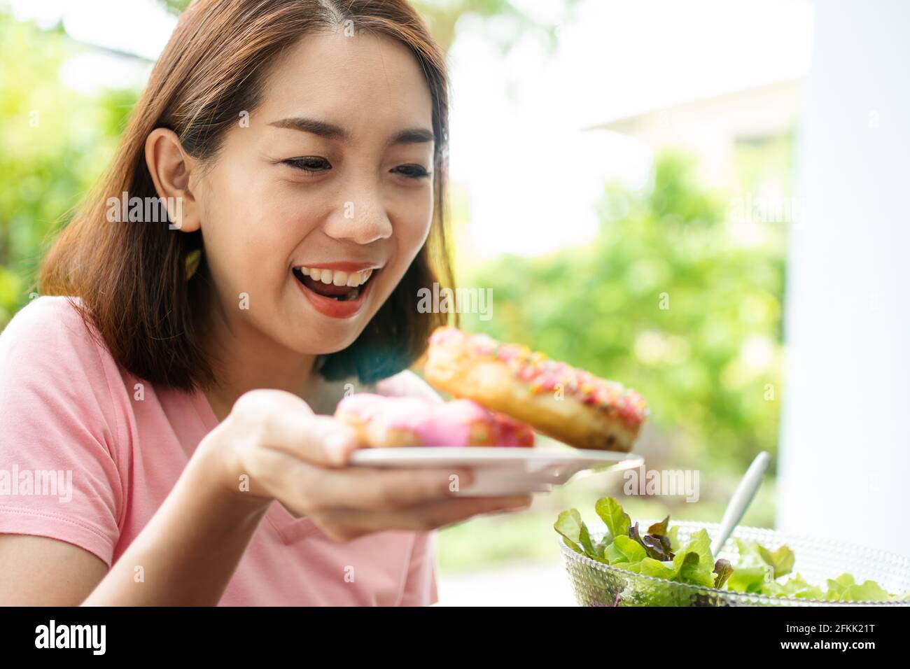 La bella donna asiatica sana di mezza età è felice di mangiare le ciambelle perché non hanno mangiato per molto tempo perché sta sperando per la salute. Concetto o Foto Stock