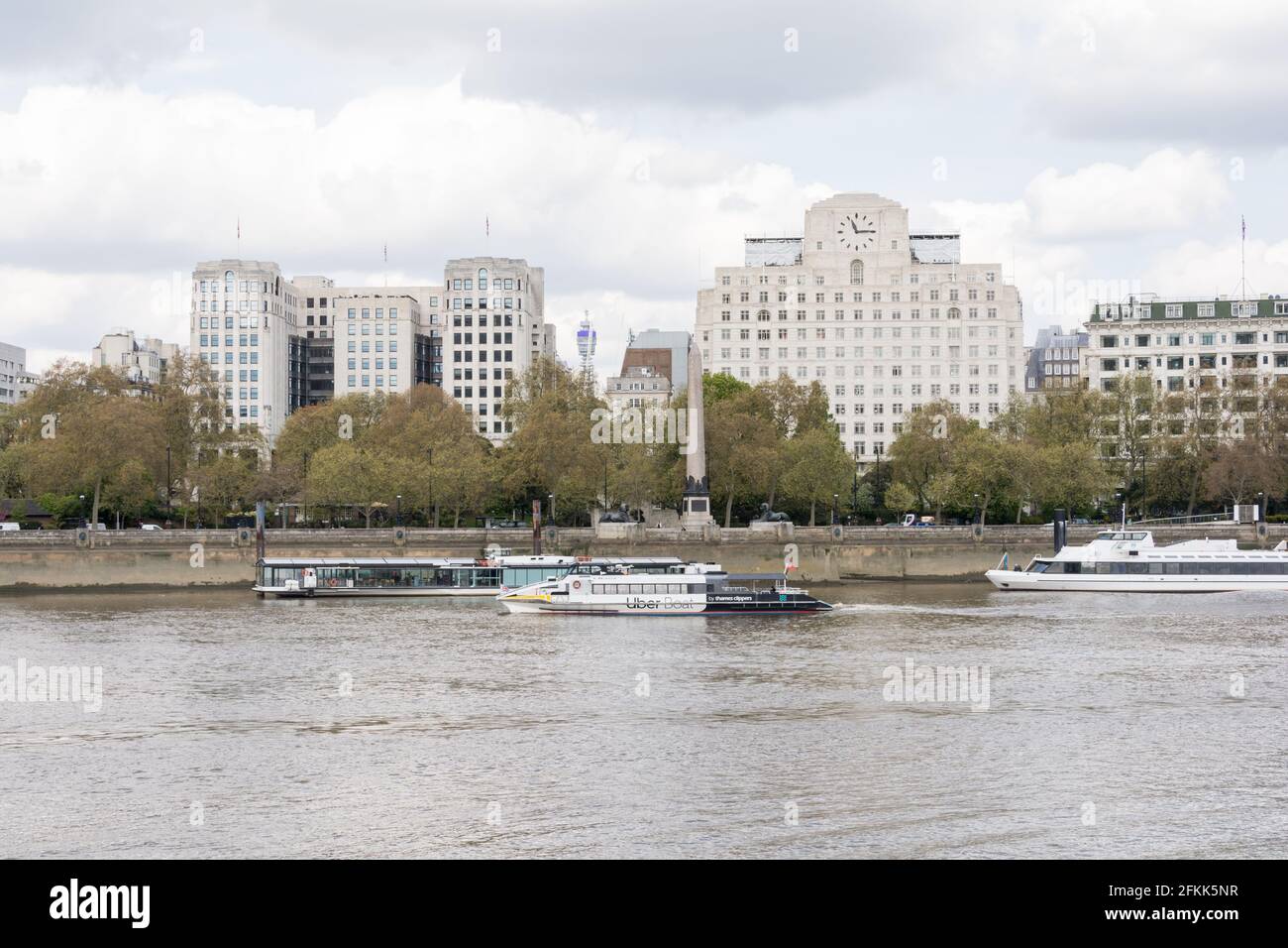 Un Tamigi Clipper Uber Boat che passa di fronte alla Shell House e Cleopatra's Needle sul Victoria Embankment, Londra, Inghilterra, Regno Unito Foto Stock