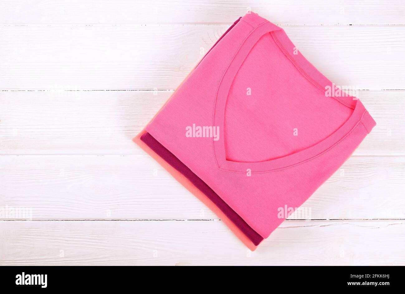 Pila di t-shirt colorate perfettamente piegate v collo su sfondo bianco tavola texture legno. Pile di diverse camicie e pullover color pastello. Arretramento Foto Stock