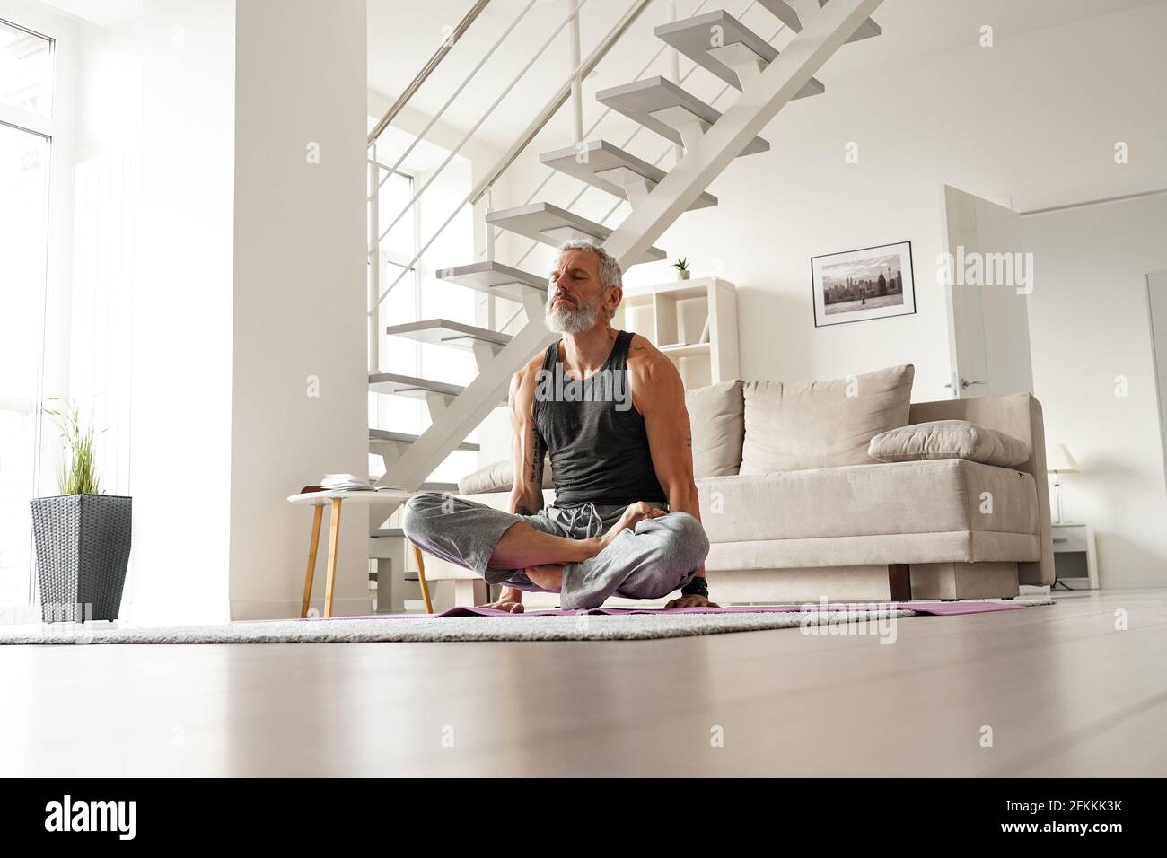 Forte più vecchio di metà età tatooed Yogi uomo facendo esercizi di yoga a casa. Foto Stock