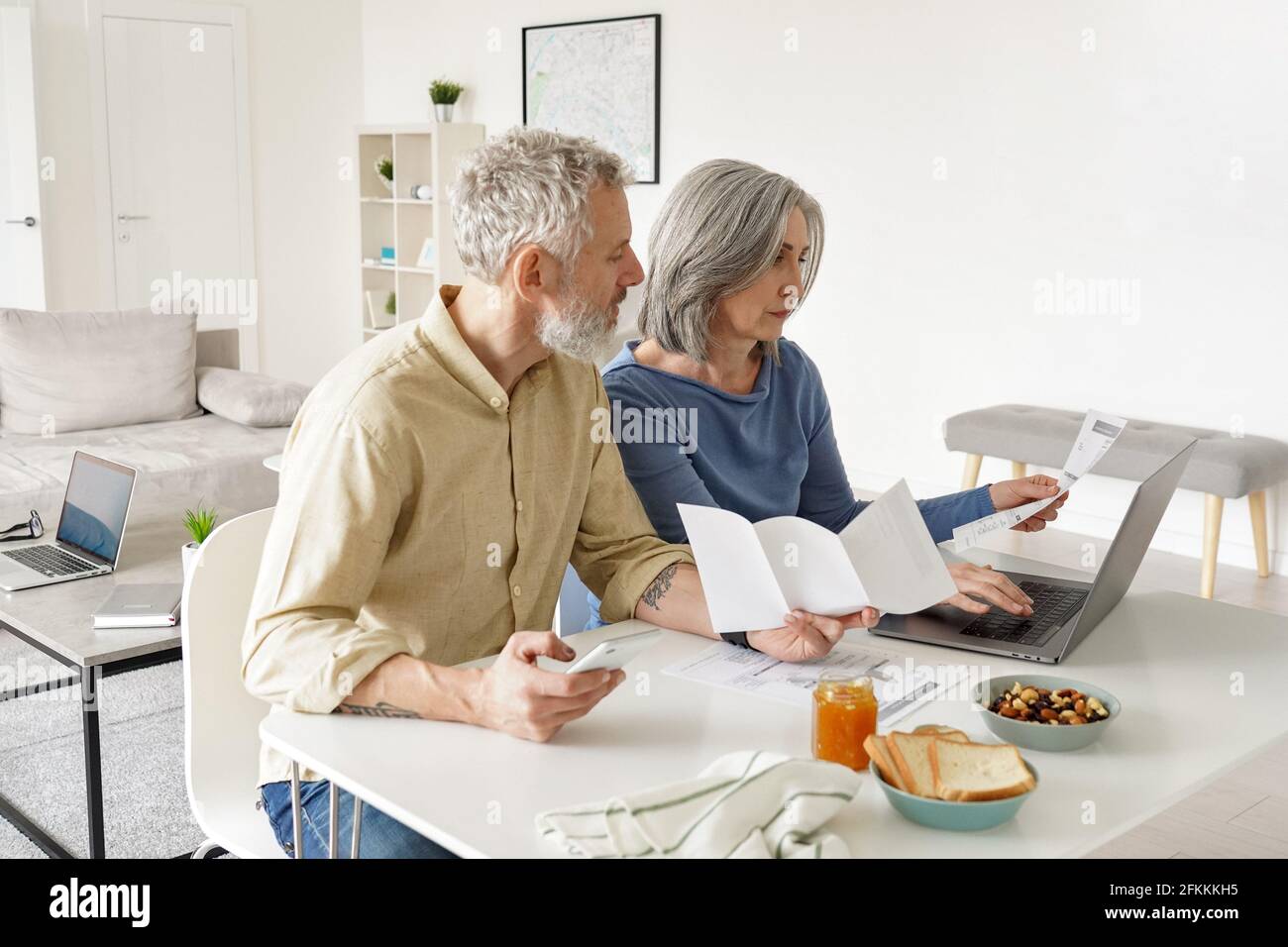 Coppia di età media che paga le fatture finanziarie in linea usando il calcolatore a casa. Foto Stock