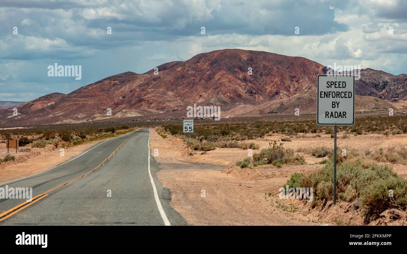 Limite di velocità 55 MPH. Velocità imposta dal radar. Indicazioni stradali di avvertenza in un'autostrada del deserto. Nevada, USA, vuota strada panoramica asfaltata, cielo nuvoloso backgroun Foto Stock