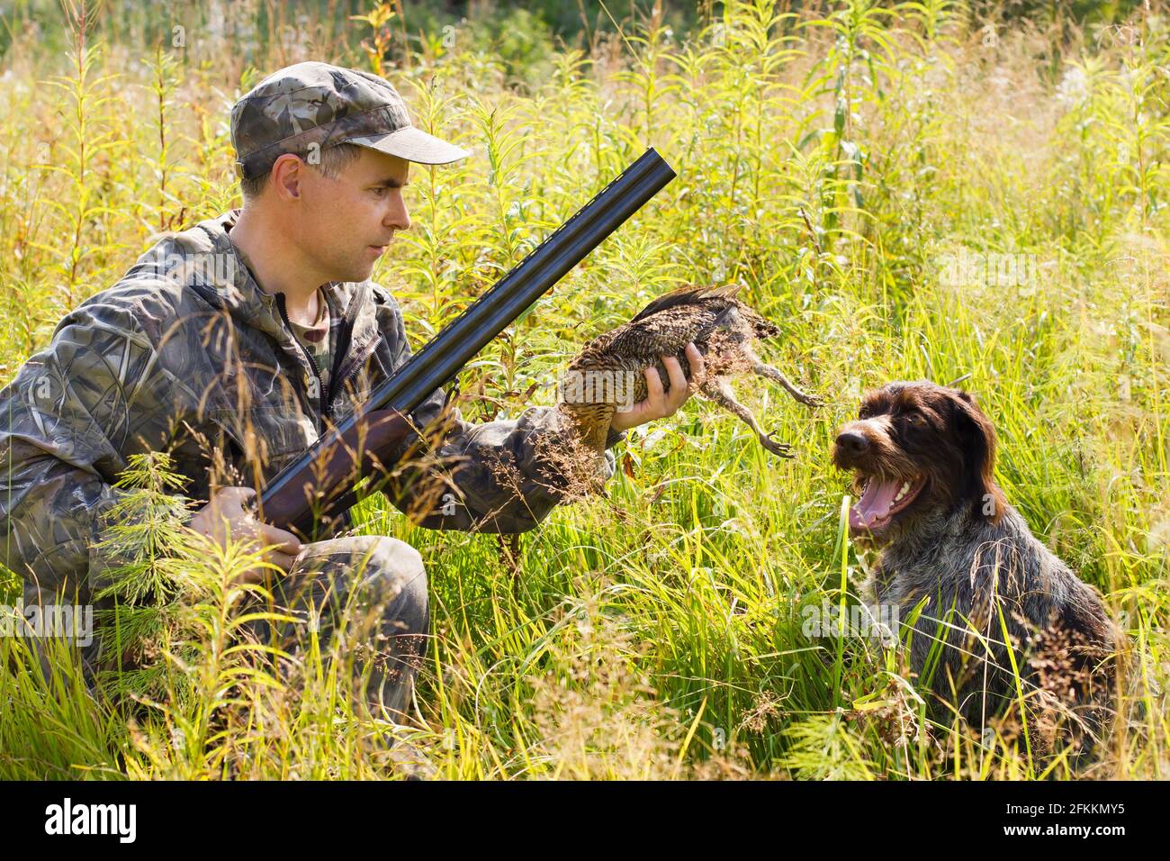 hunter che tiene un guuso abbattuto, che ha portato il gundog (puntatore con i capelli tedeschi) durante la caccia Foto Stock